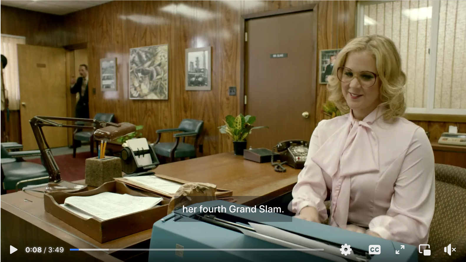 Amy Schumer in character as a 1970s secretary. The closed caption reads "her fourth Grand Slam."