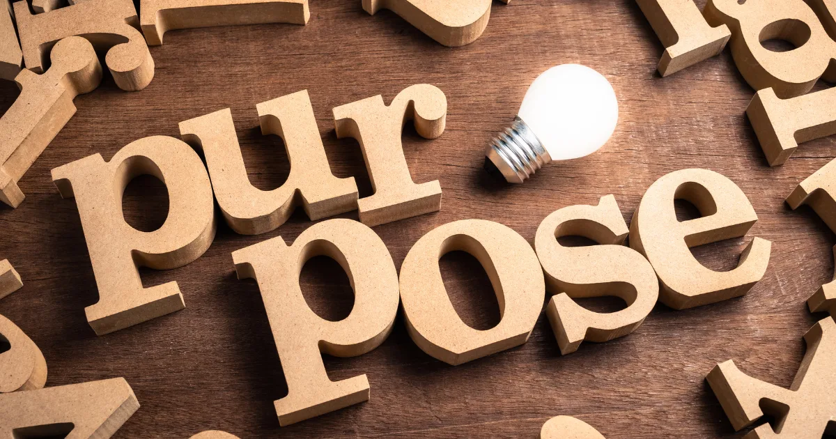 Wooden table with wooden letters spelling out purpose. There is a lightbulb beside it.